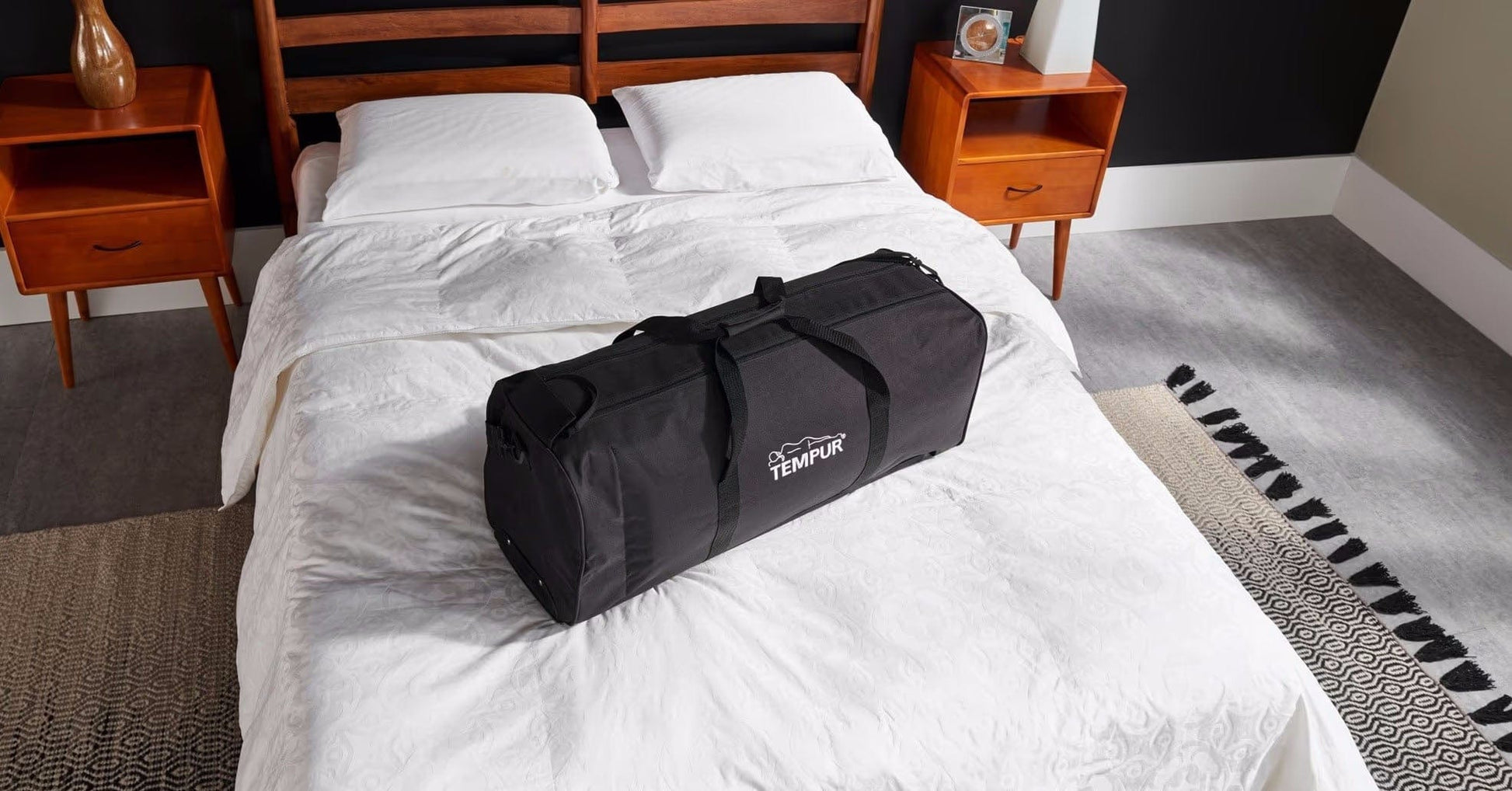 The Tempur-Pedic Travel Set neatly packed in its durable black carrying case, placed on a stylish bed with white bedding, showcasing its compact and portable design for convenient travel.